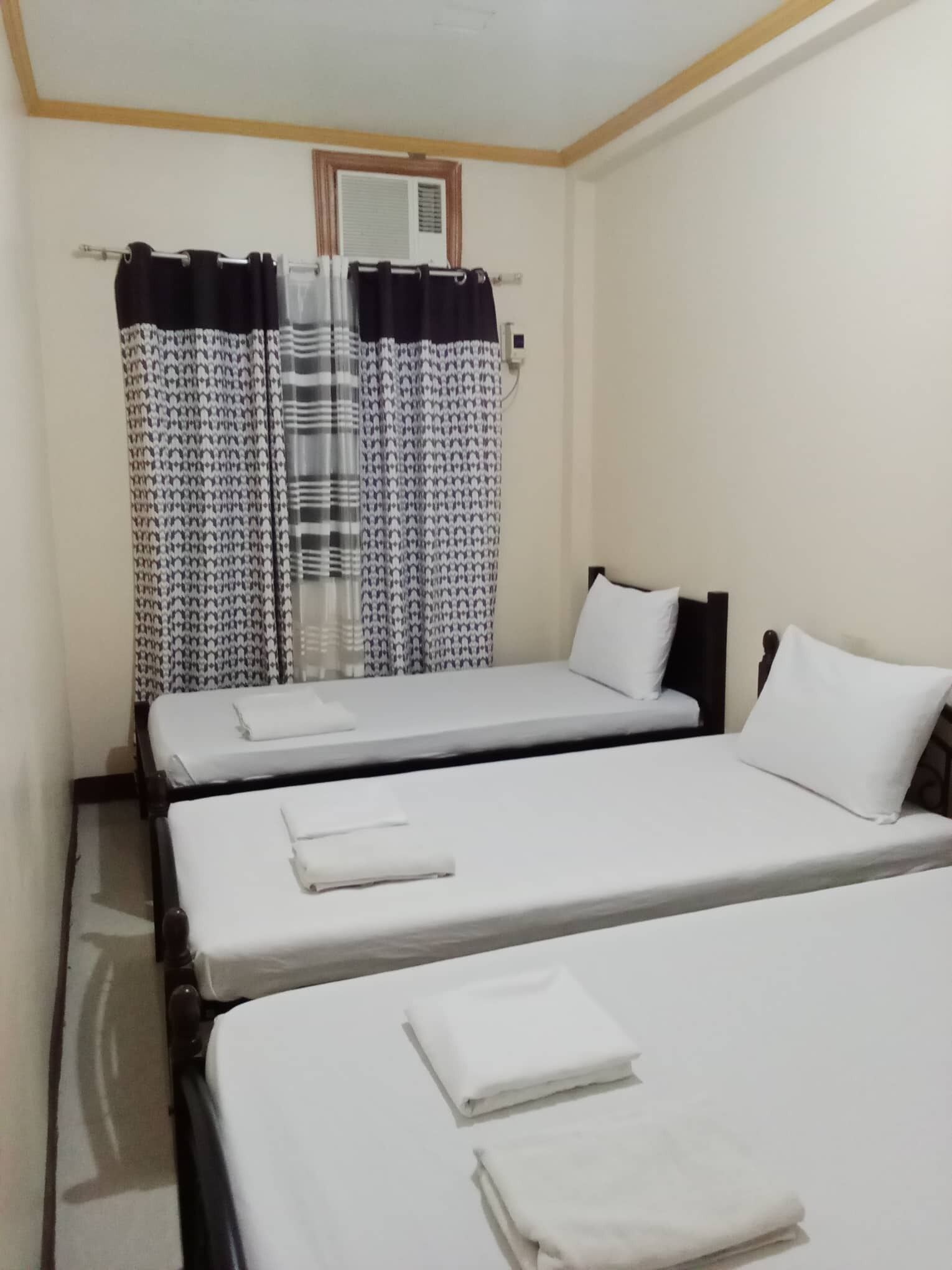 A hotel room with two single beds, a window with patterned curtains, and a wall-mounted air conditioning unit.