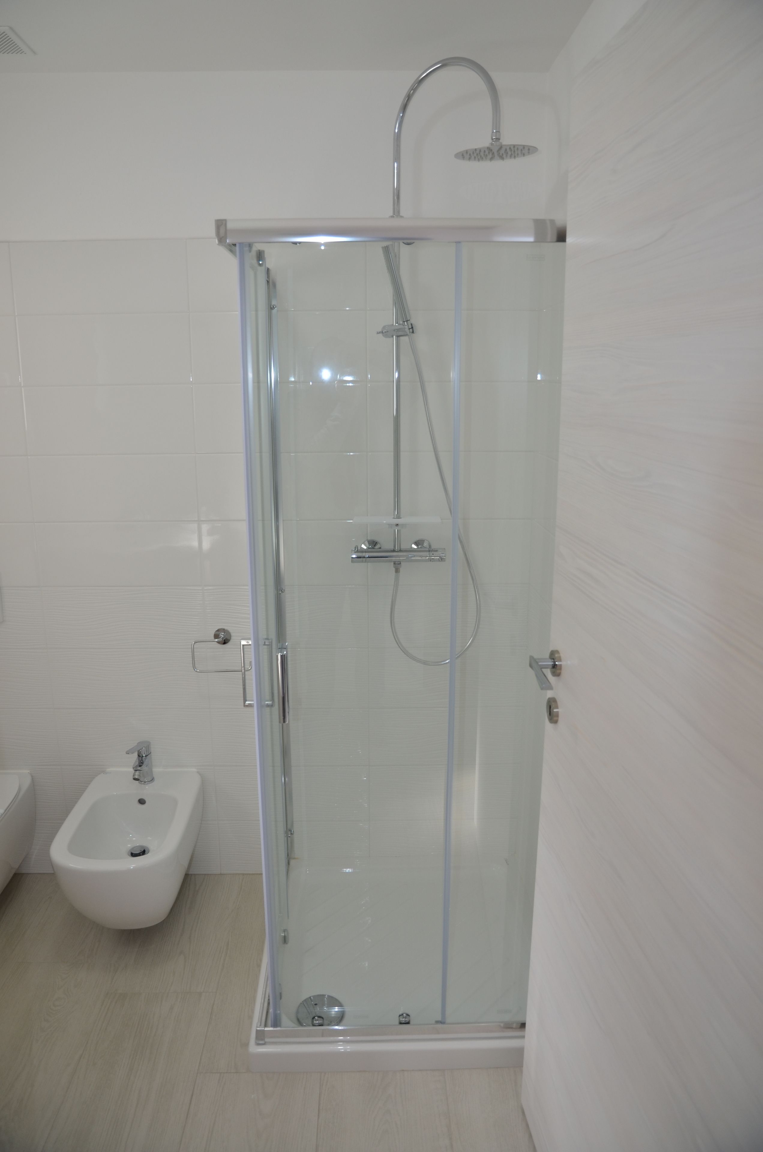 Une salle de bain moderne dotée d’une douche à parois de verre, d’un bidet et d’un sol carrelé.