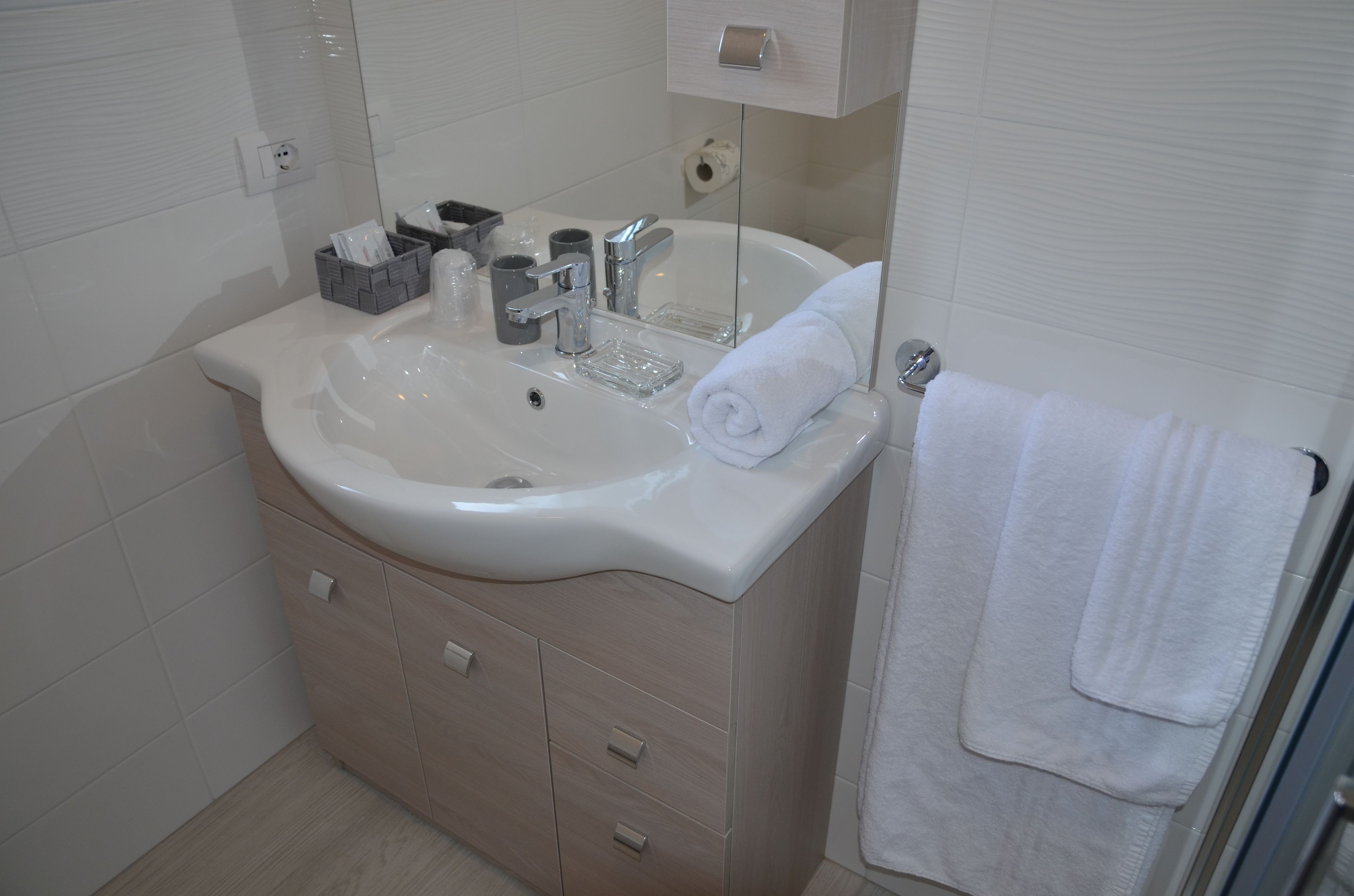 A bathroom with a white sink, a mirror, a towel hanging on the wall, and a wooden cabinet with drawers.