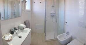 A modern bathroom with a glass-enclosed shower, a bidet, and a sink with toiletries. - Crystal bed and breakfast (Dormelletto)
