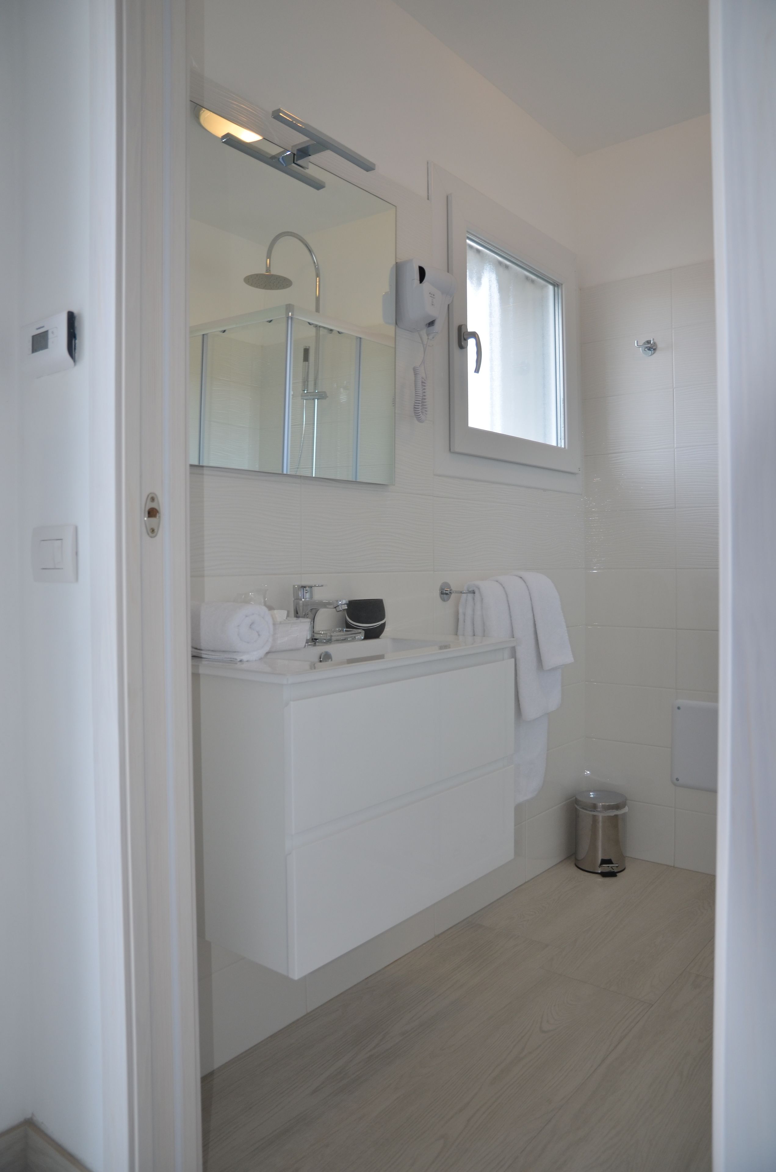 Une salle de bain moderne avec une douche à parois de verre, un meuble-lavabo blanc avec un miroir et une petite poubelle.