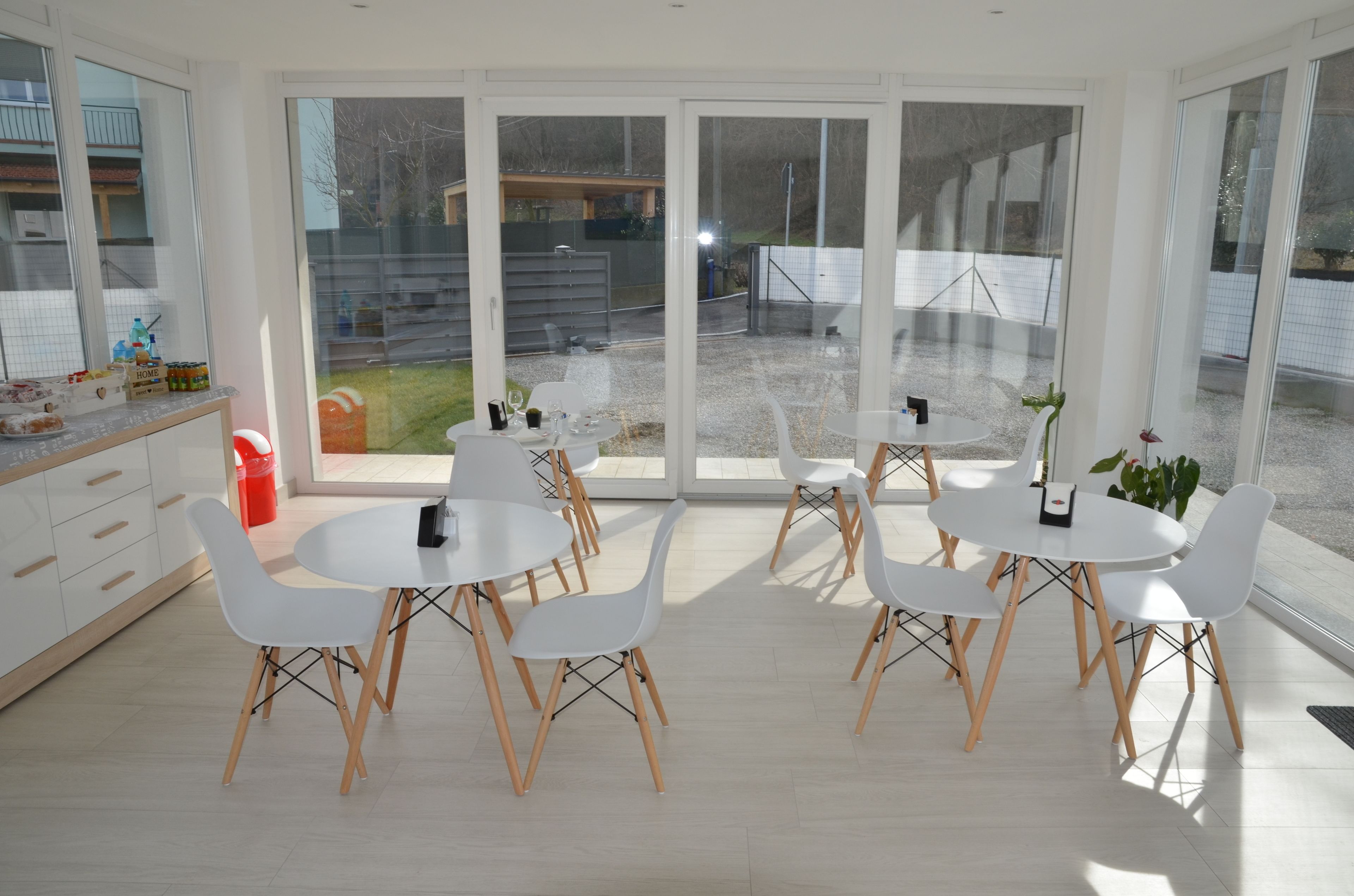A modern kitchen with white cabinets, a dining area with white chairs and tables, and large sliding glass doors leading to a backyard.