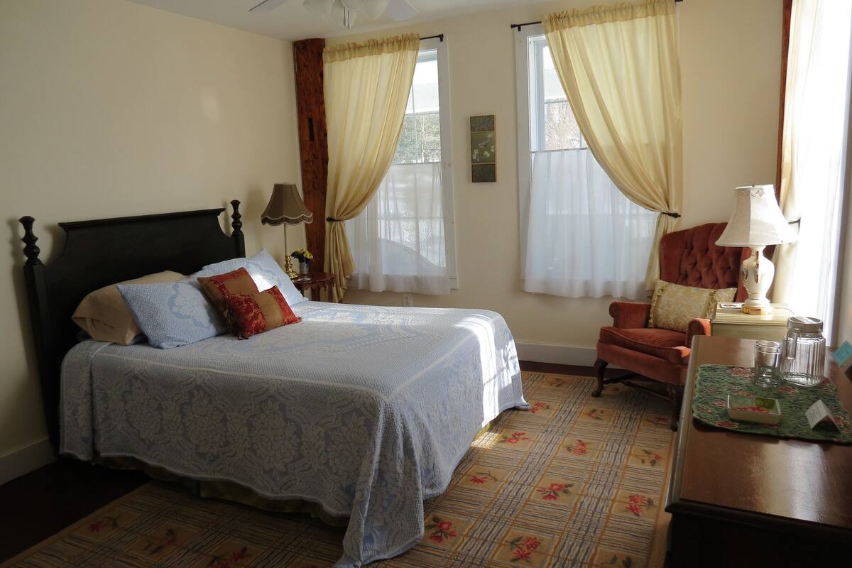 Une chambre à coucher avec un lit, une chaise, une table et une lampe.