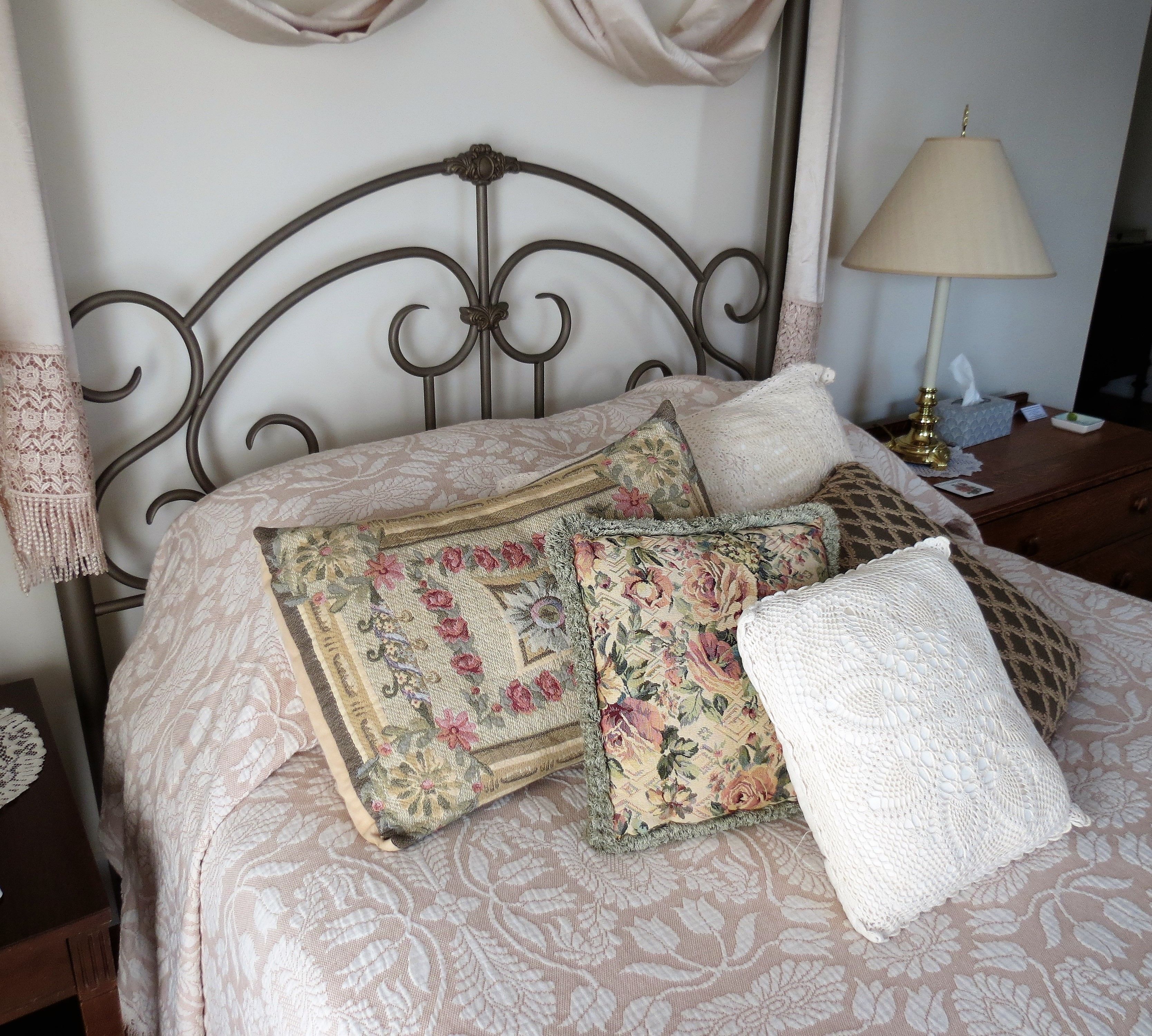 A bed with floral-patterned bedding and multiple pillows, a bedside lamp, and a lace doily on the nightstand.