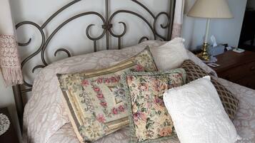 A bed with floral-patterned bedding and multiple pillows, a bedside lamp, and a lace doily on the nightstand.