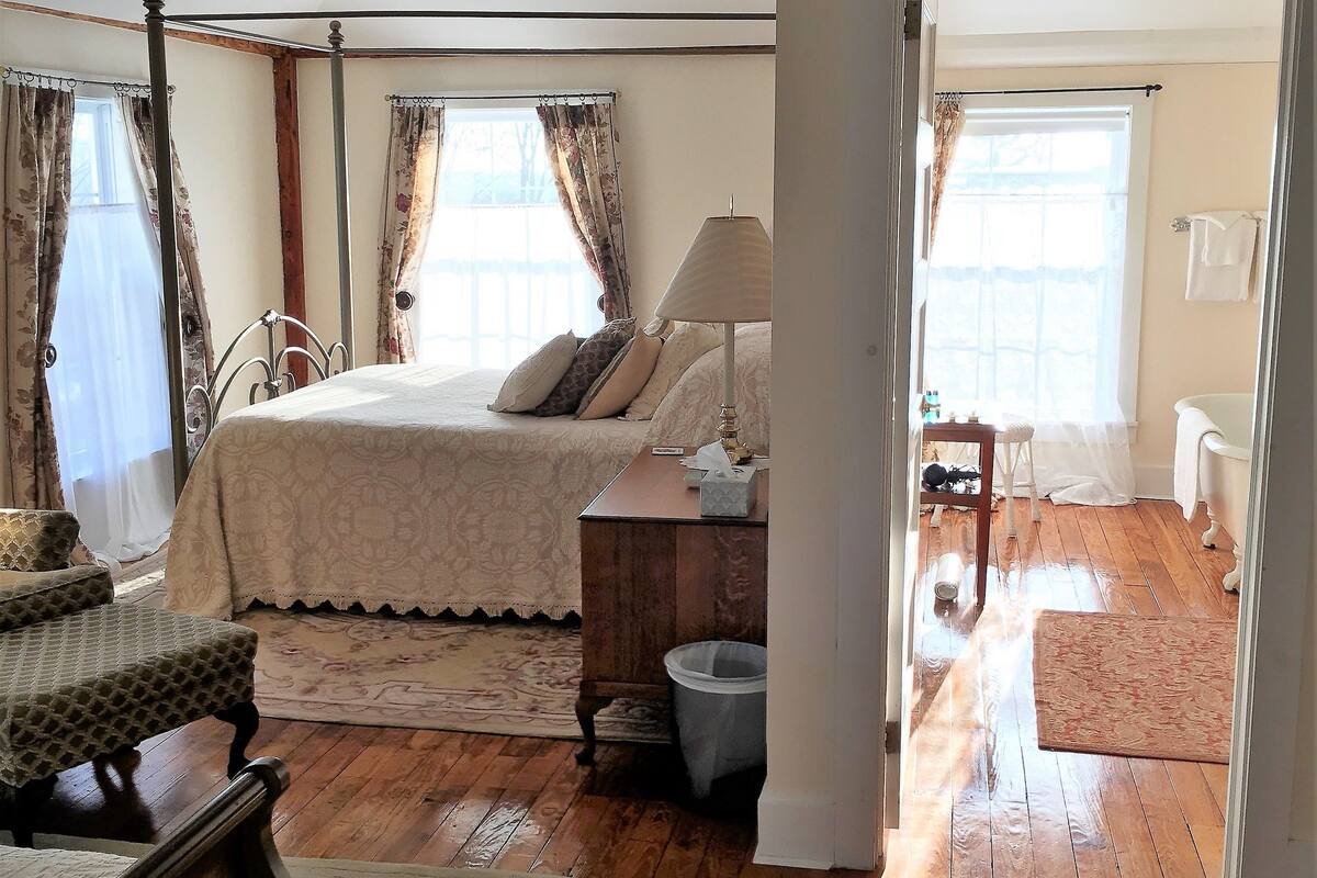 Une chambre à coucher avec un lit à baldaquin, des poutres apparentes, une table de chevet et une petite table de nuit avec une lampe.