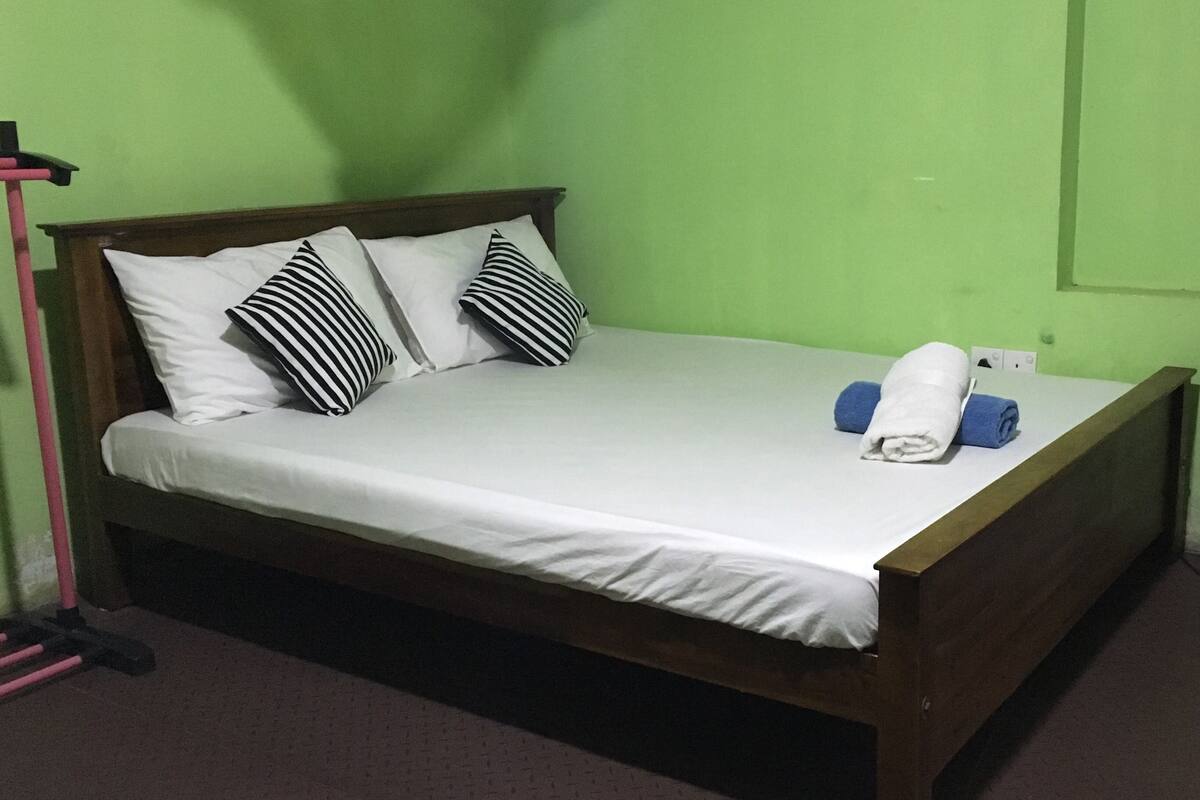 A single bed with white bedding, two black and white striped pillows, and two rolled towels (one white, one blue) on the bed.