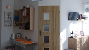 A compact kitchen with a wooden door, a small table with orange placemats, and a wall-mounted TV. - Privat Voyage (Liptovsky Mikulas)