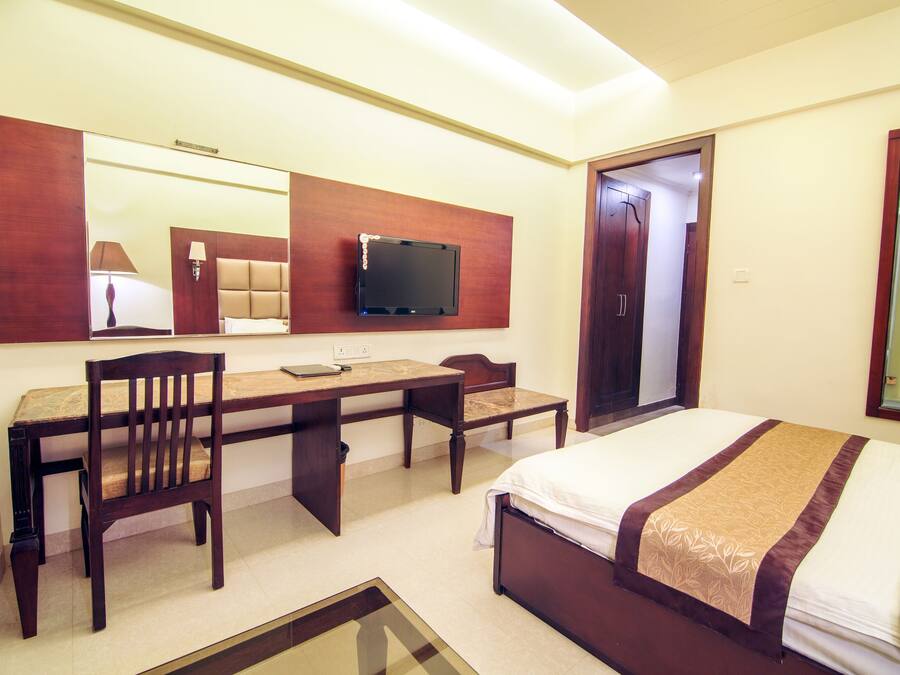 Habitación de hotel con cama, escritorio, silla, televisor montado en la pared y espejo.