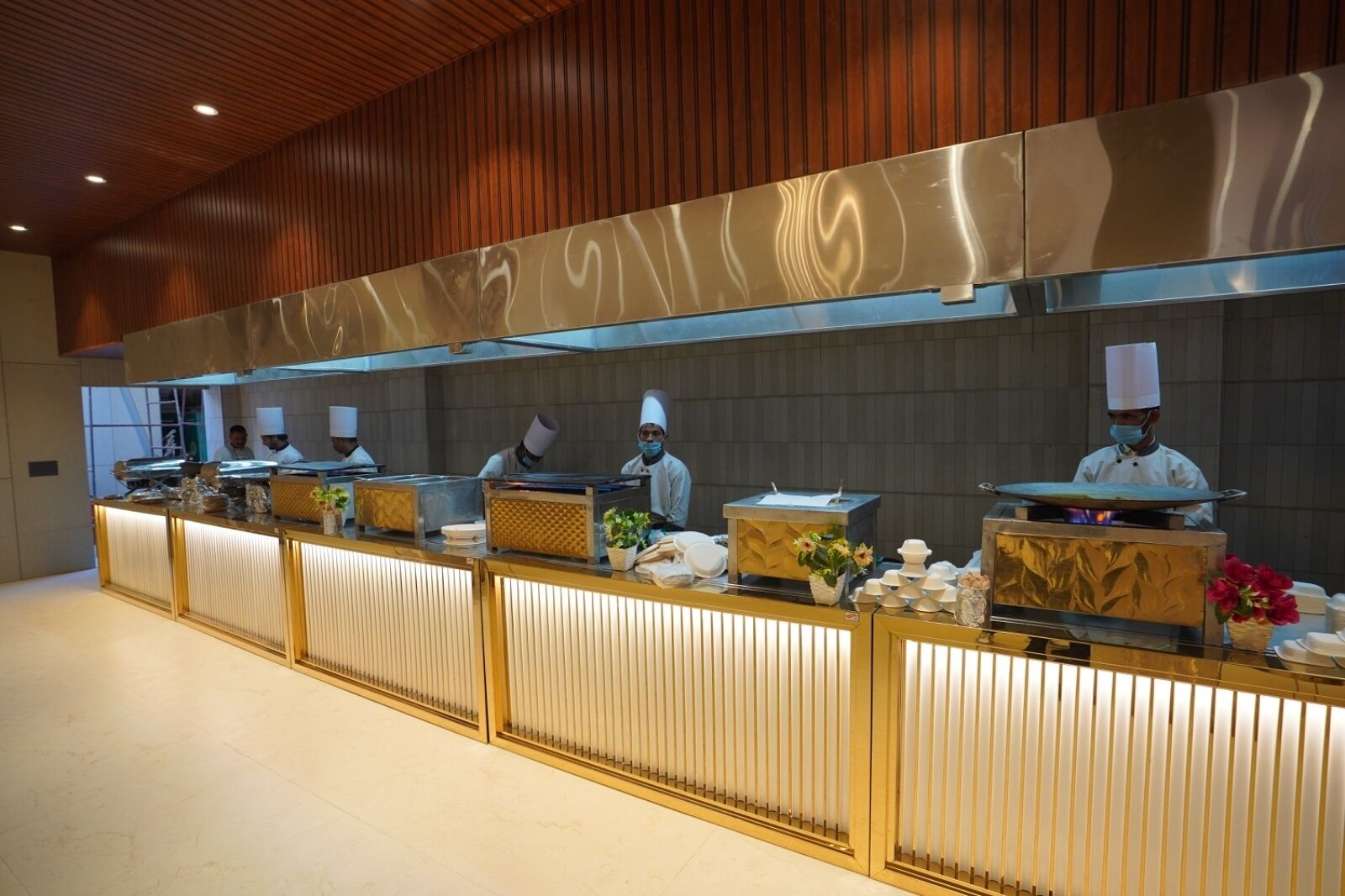 A modern kitchen with a long counter, chefs in uniform, and various kitchen equipment.