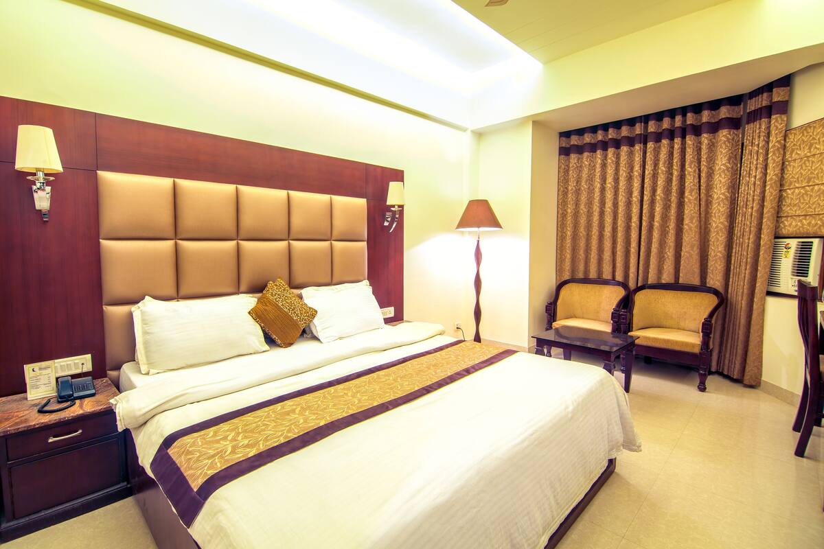 Una habitación de hotel con una cama grande, una mesita de noche con un teléfono, dos sillas y una lámpara.