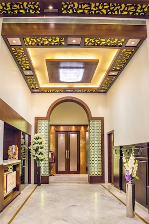 A hotel lobby with a marble floor, a reception desk, and a large arched doorway.