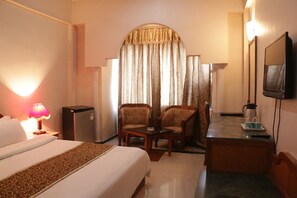 Una habitación de hotel con una cama, un escritorio, dos sillas, un televisor y una lámpara.