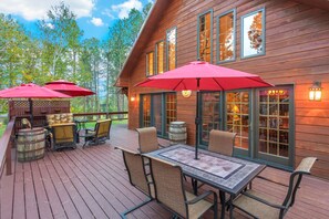 A wooden deck with outdoor furniture and umbrellas, overlooking a forested area.