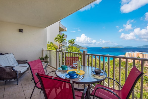 Een balkon met een tafel voor twee, met uitzicht op de kust, gebouwen en palmbomen.