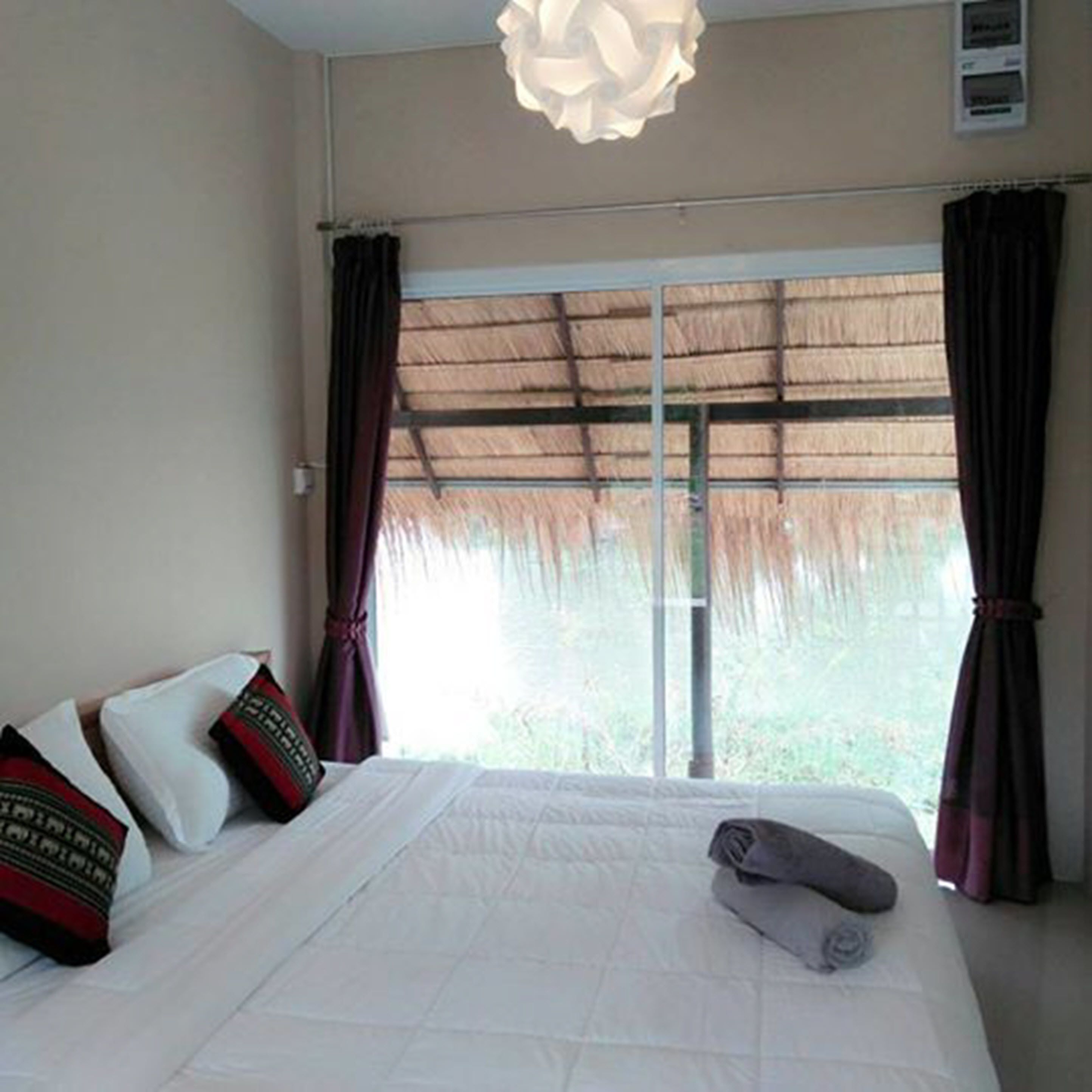 A hotel room with a bed, a large window with curtains, and a ceiling light fixture.