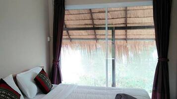 A hotel room with a bed, a large window with curtains, and a ceiling light fixture.