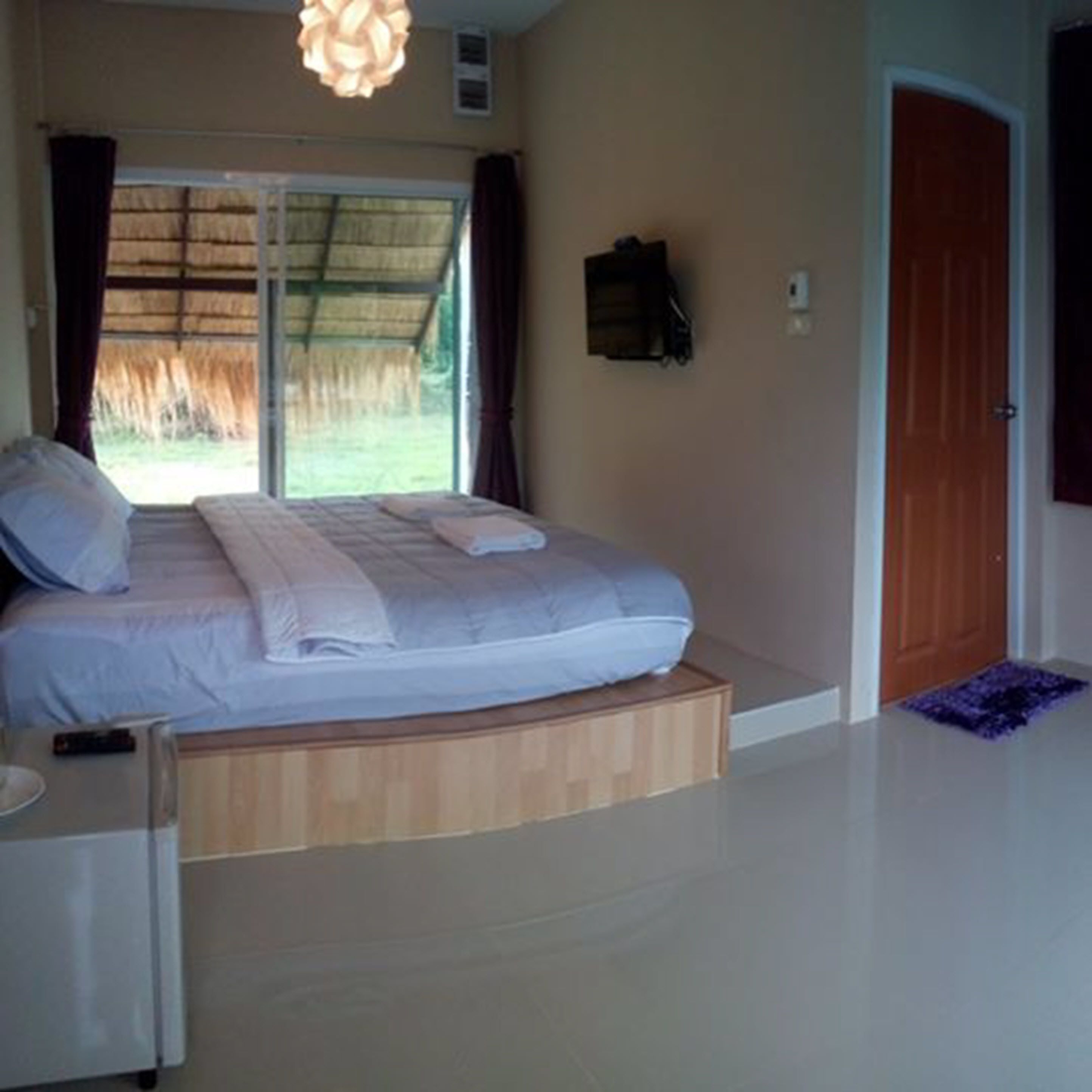 A bedroom with a bed, a small table, a heater, a door, and a window with curtains.