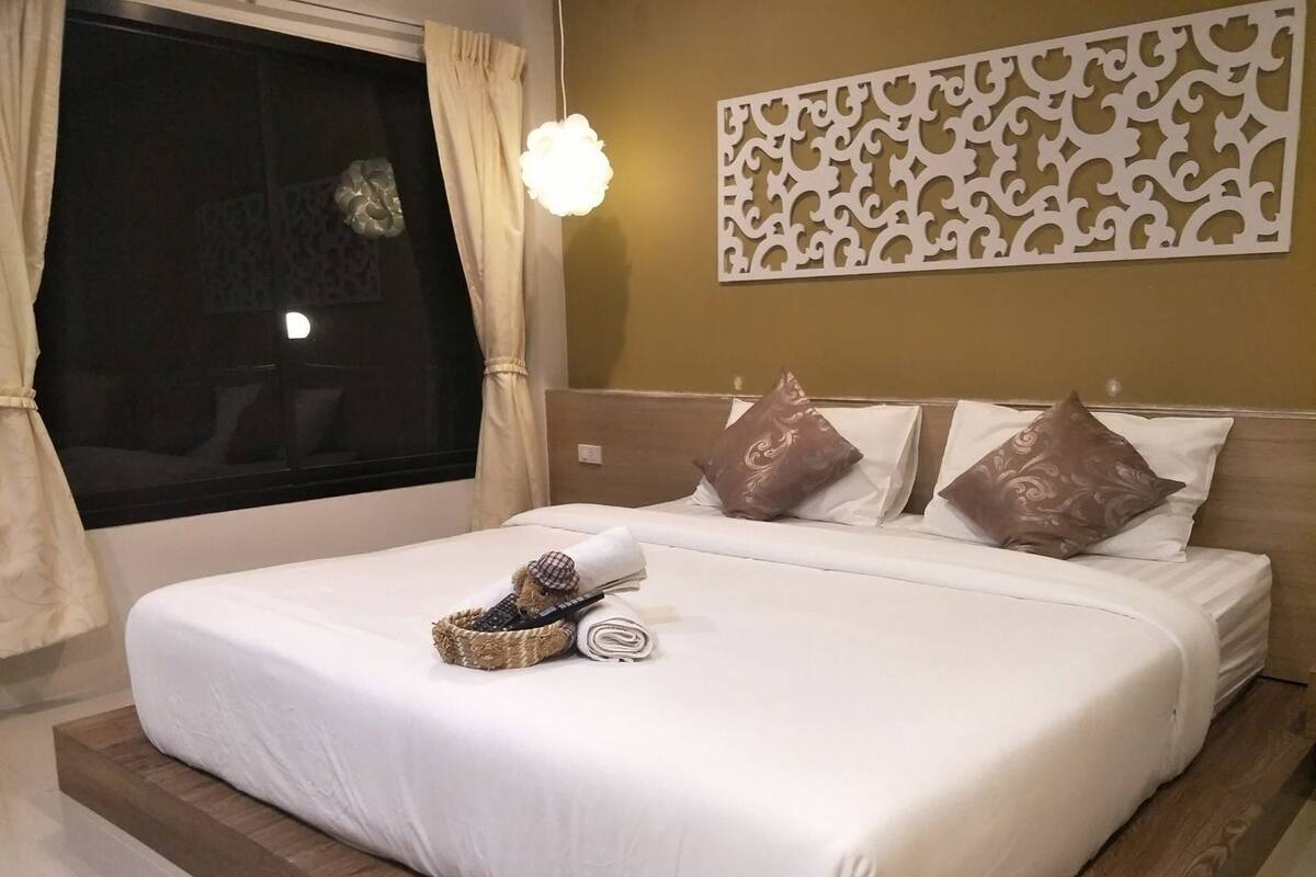 Ein Hotelzimmer mit einem großen Bett, einem Fenster mit Vorhängen, einer Wandverkleidung und einer Nachttischlampe.