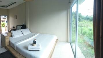 Una camera d'albergo con un letto grande, un comodino, una sedia, una finestra con vista sul verde e una porta che dà su un balcone.