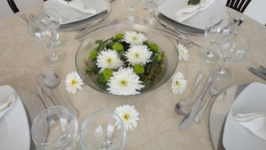 A round dining table set for four with white plates, clear glassware, and a centerpiece of white flowers and green leaves. - Wonderful Penthouse  (Funchal)