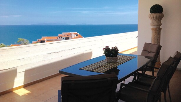 A balcony with a table and chairs, overlooking a coastal view with buildings and the sea. - Wonderful Penthouse  (Funchal)