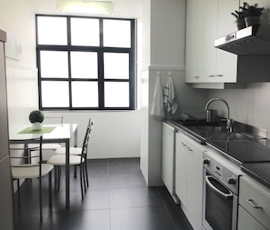 A compact kitchen with a dining table, chairs, a window, a sink, and an oven.