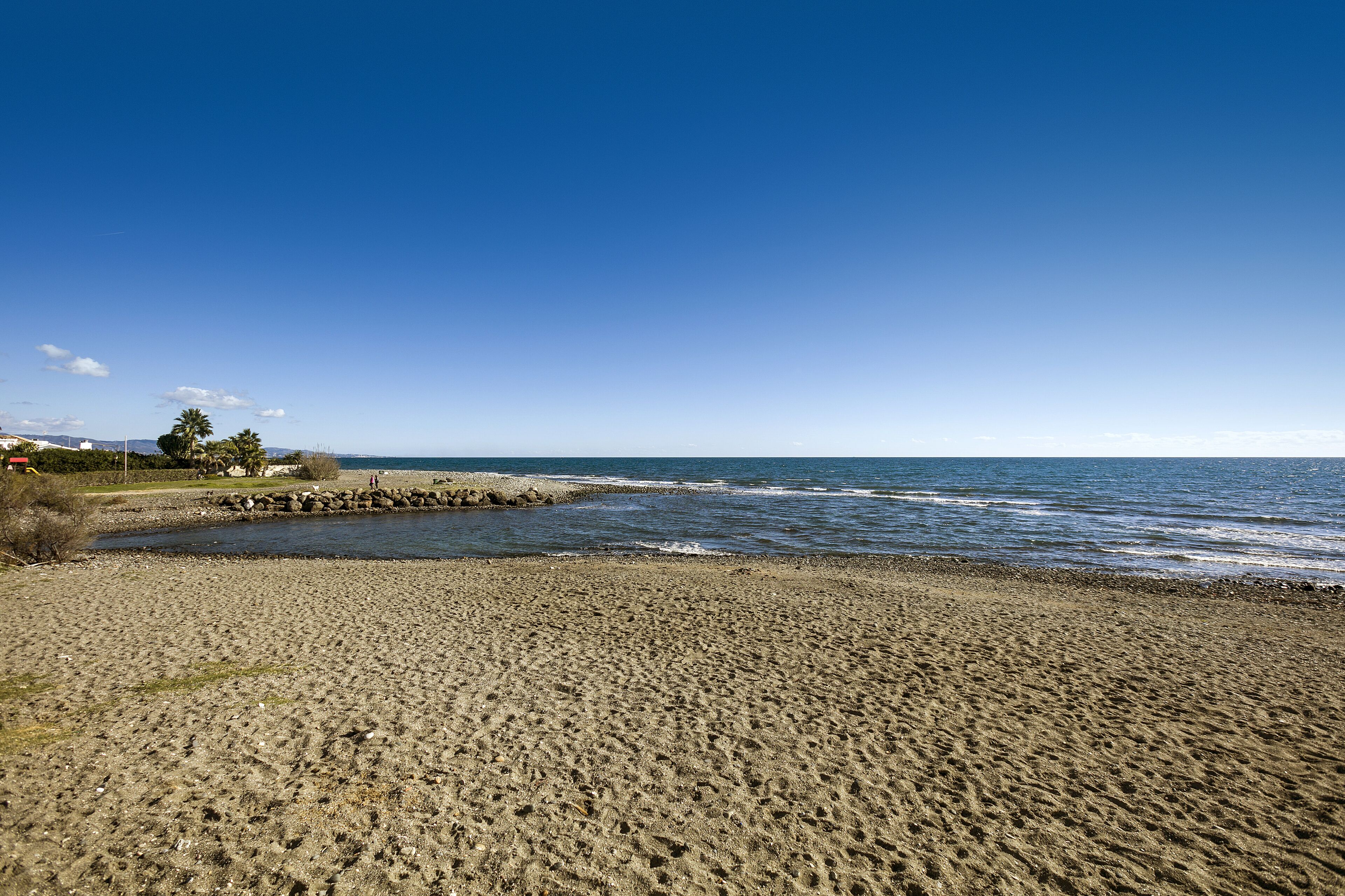 A beach with a rocky shoreline, clear blue sky, and calm sea.