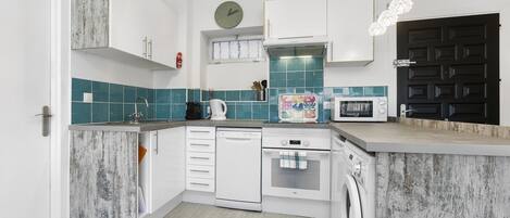A modern kitchen with white cabinetry, a dishwasher, an oven, a microwave, and a washing machine.