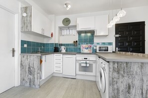 Eine moderne Küche mit weißen Schränken, einem Geschirrspüler, einem Backofen, einer Mikrowelle und einer Waschmaschine.