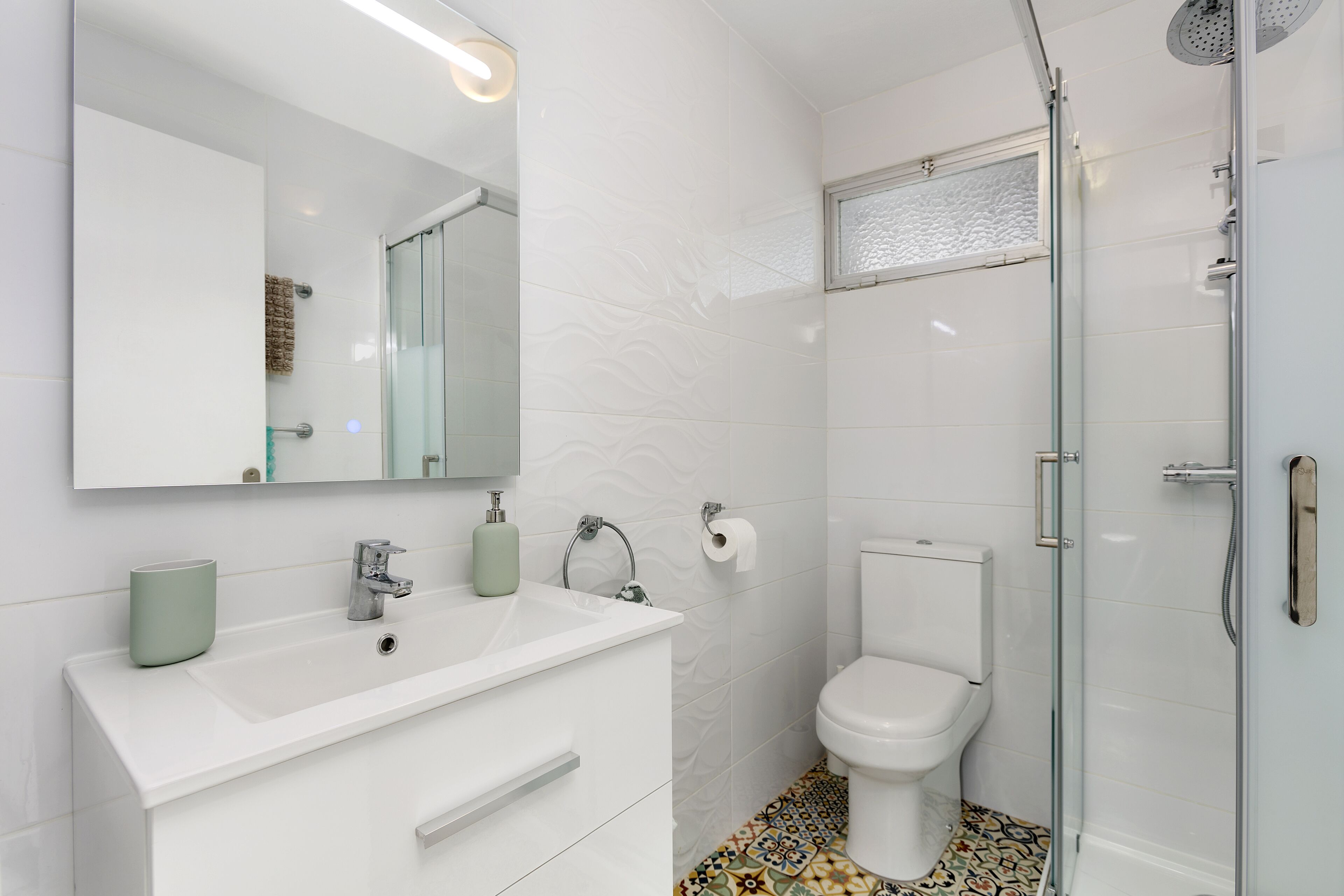 A modern bathroom with a white sink, mirror, and toilet.