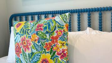 Een bed met een blauw hoofdeinde, een kleurrijk bloemenkussen en een wit kussen.
