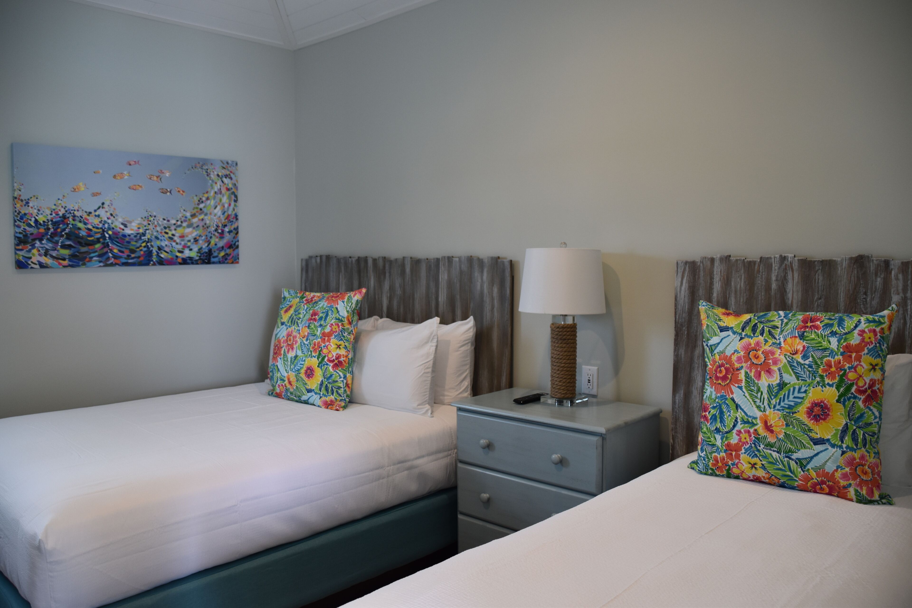 Habitación de hotel con dos camas, una mesita de noche, una lámpara y un cuadro en la pared.