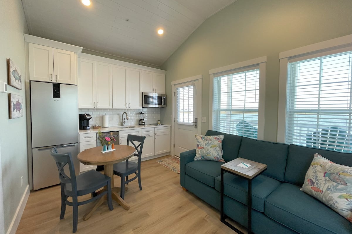 A compact living space with a kitchenette, a dining area with a table and chairs, and a sofa with decorative pillows.