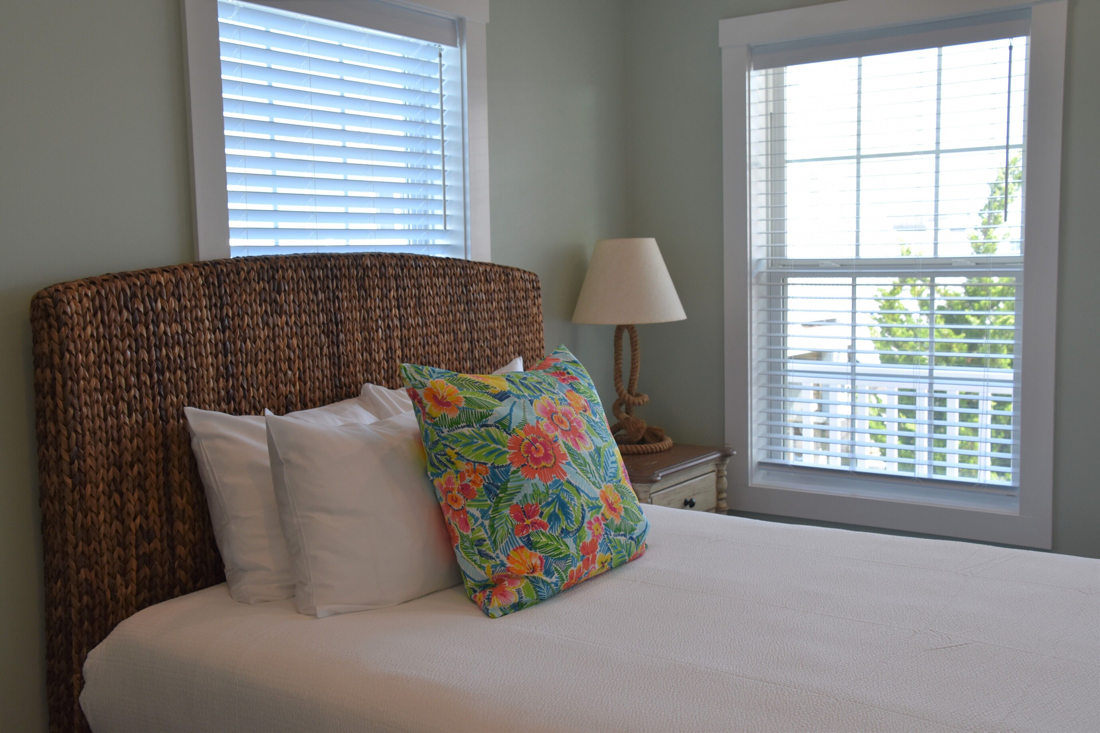 A bed with a woven headboard, white bedding, and a colorful floral pillow.
