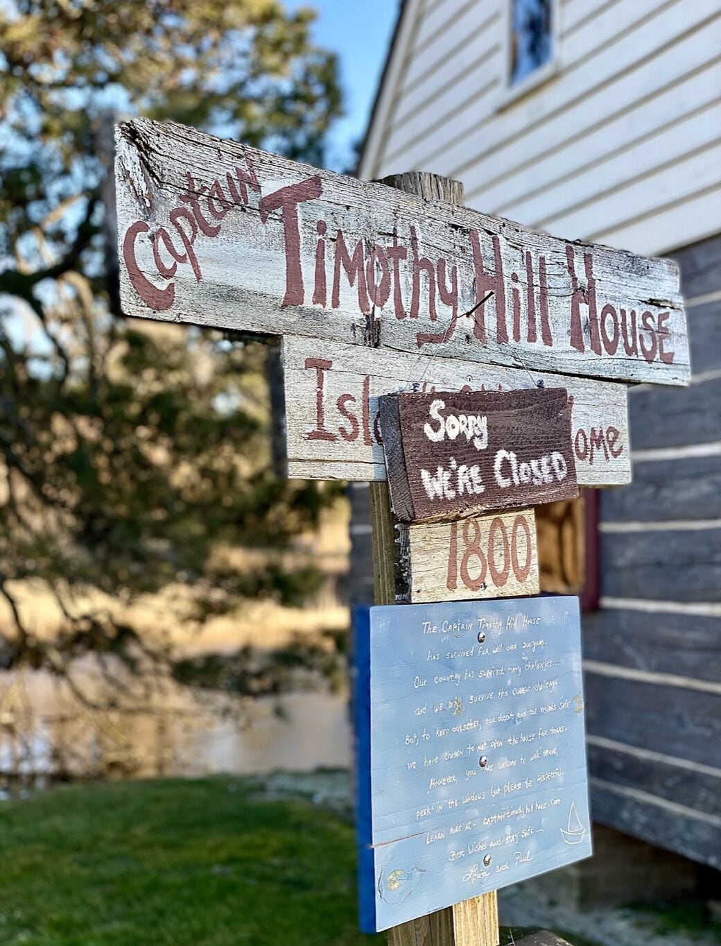 A wooden signpost with 'Captain Timothy Hill House' and 'Sorry we're closed' signs, and a small informational board below.