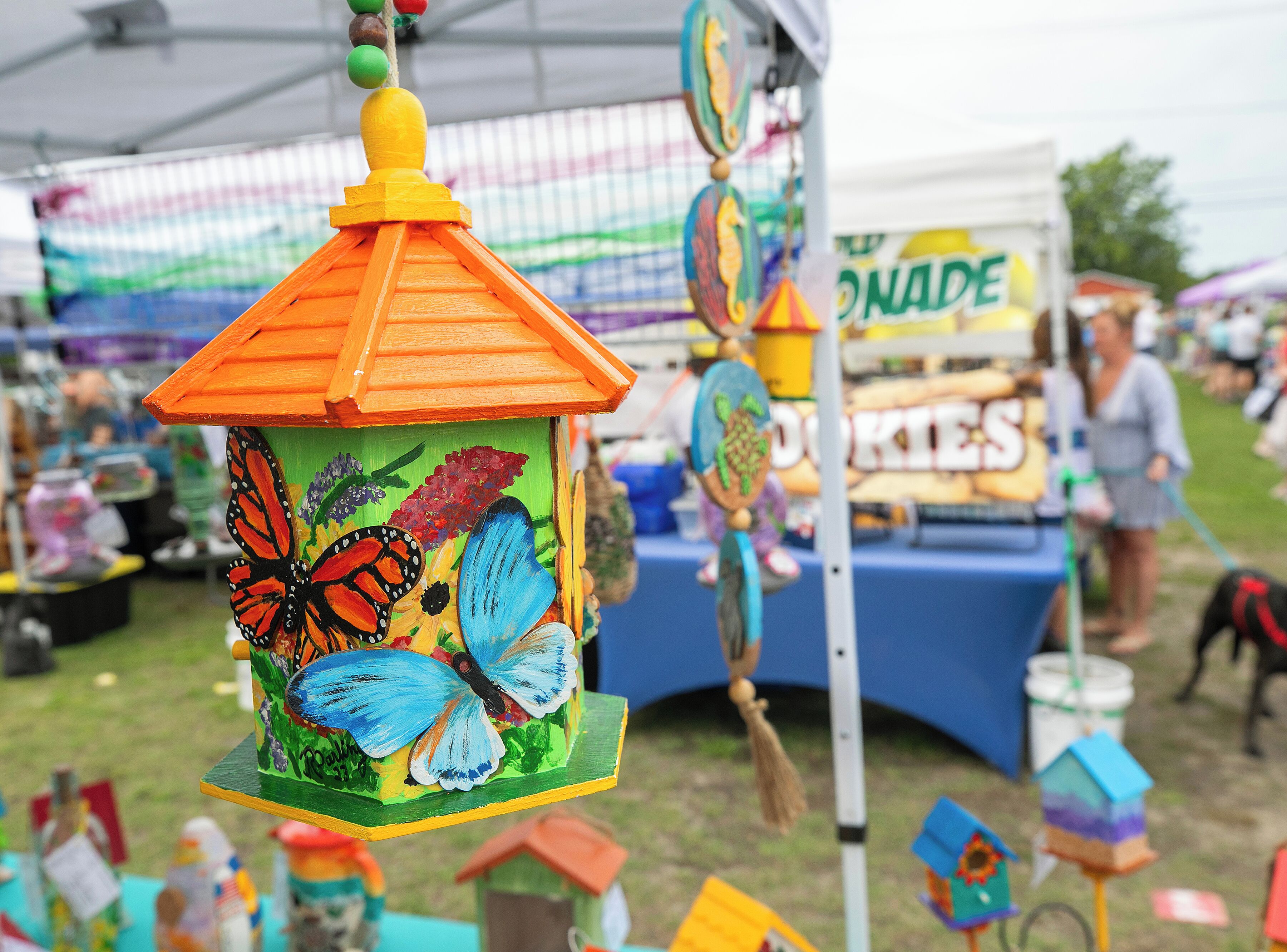 A colorful birdhouse with painted butterflies, a tent, and a food stall in the background.