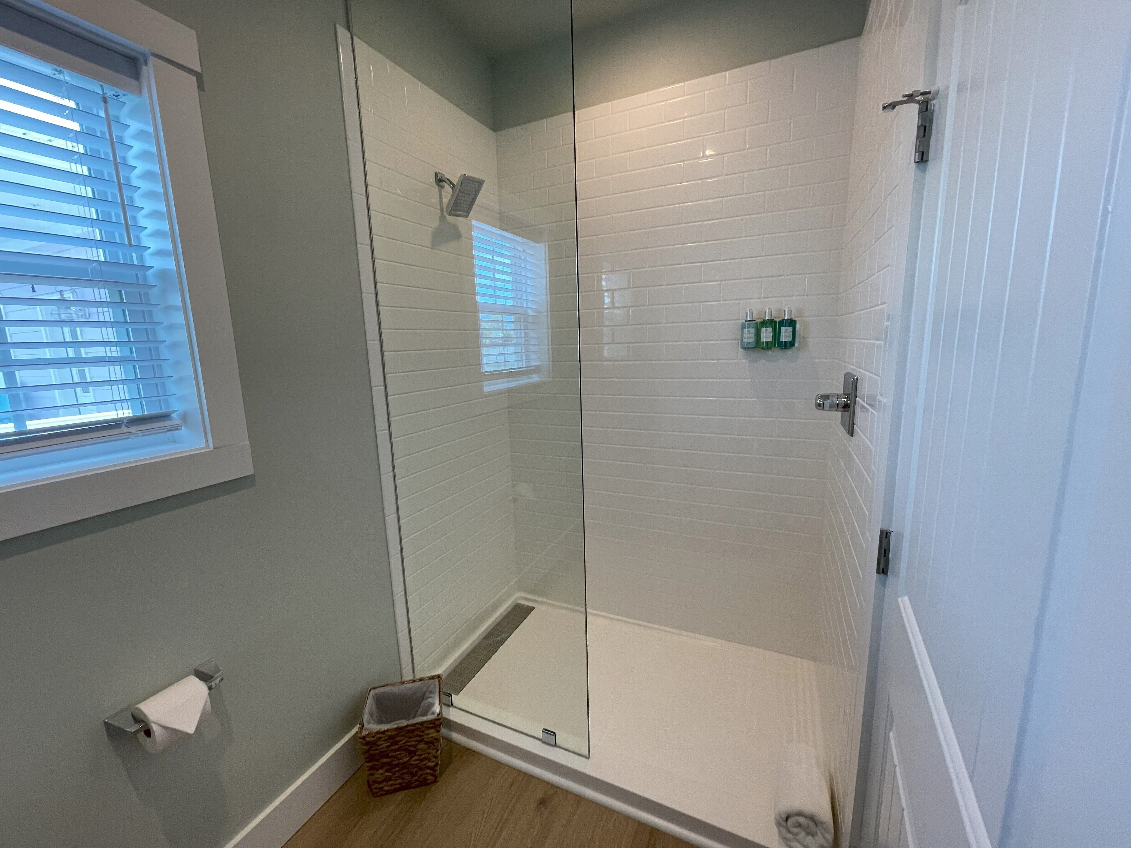 A modern bathroom with a glass shower enclosure, a toilet paper holder, and a small basket.