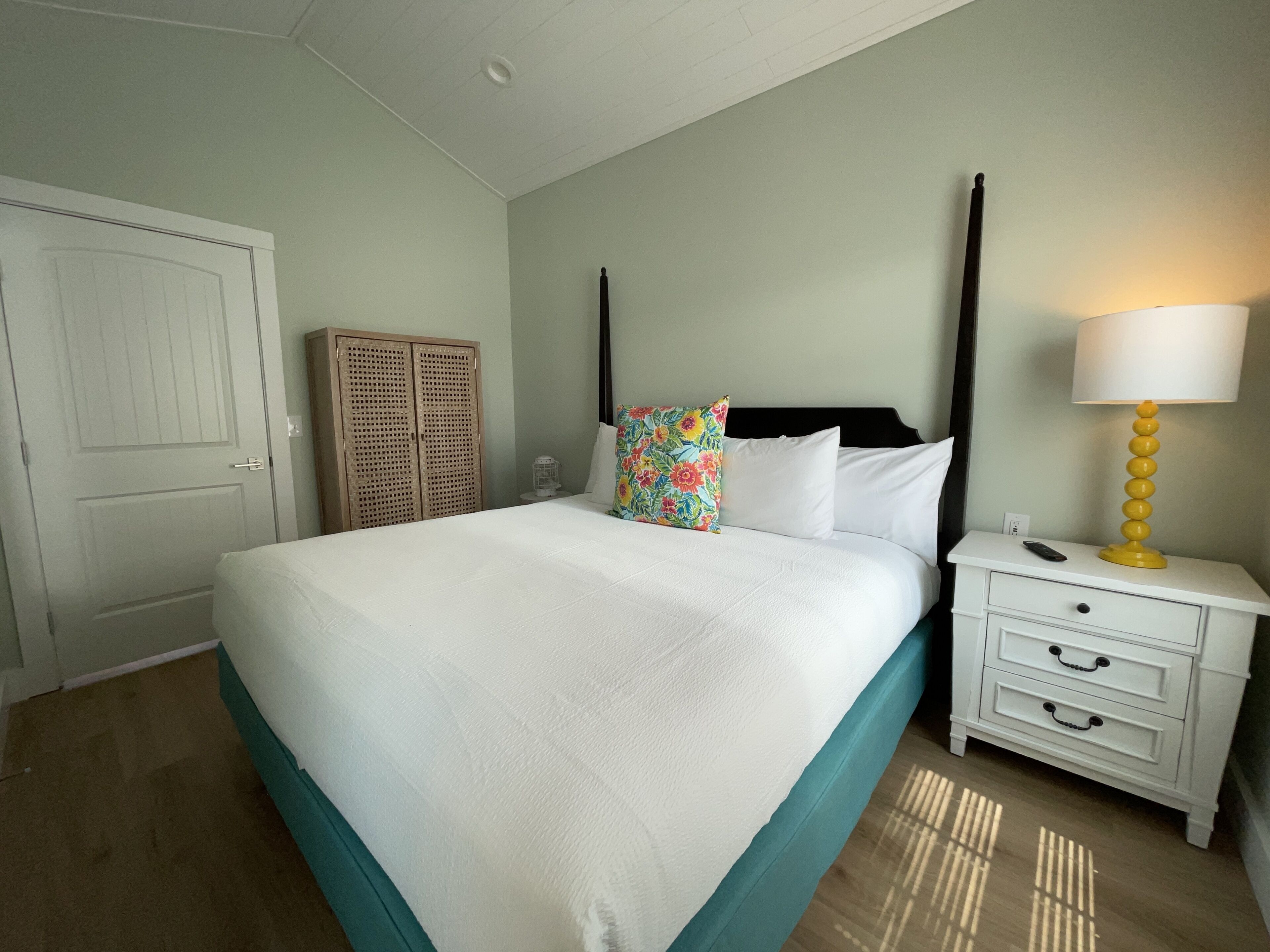 A bedroom with a bed, a nightstand, a lamp, a wardrobe, and a door.