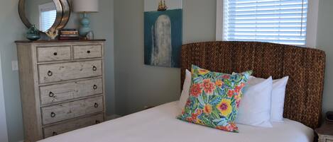 Een slaapkamer met een bed, een kaptafel, een spiegel, een lamp en een schilderij van een schip en walvis.