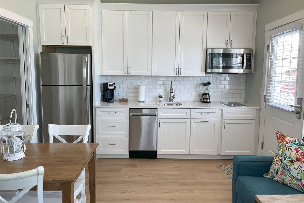 A modern kitchen with white cabinets, stainless steel appliances, and a wooden dining table.
