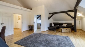 Un loft espacioso con techo alto, vigas de madera expuestas, un sofá de cuero negro, un cofre de madera y una araña.