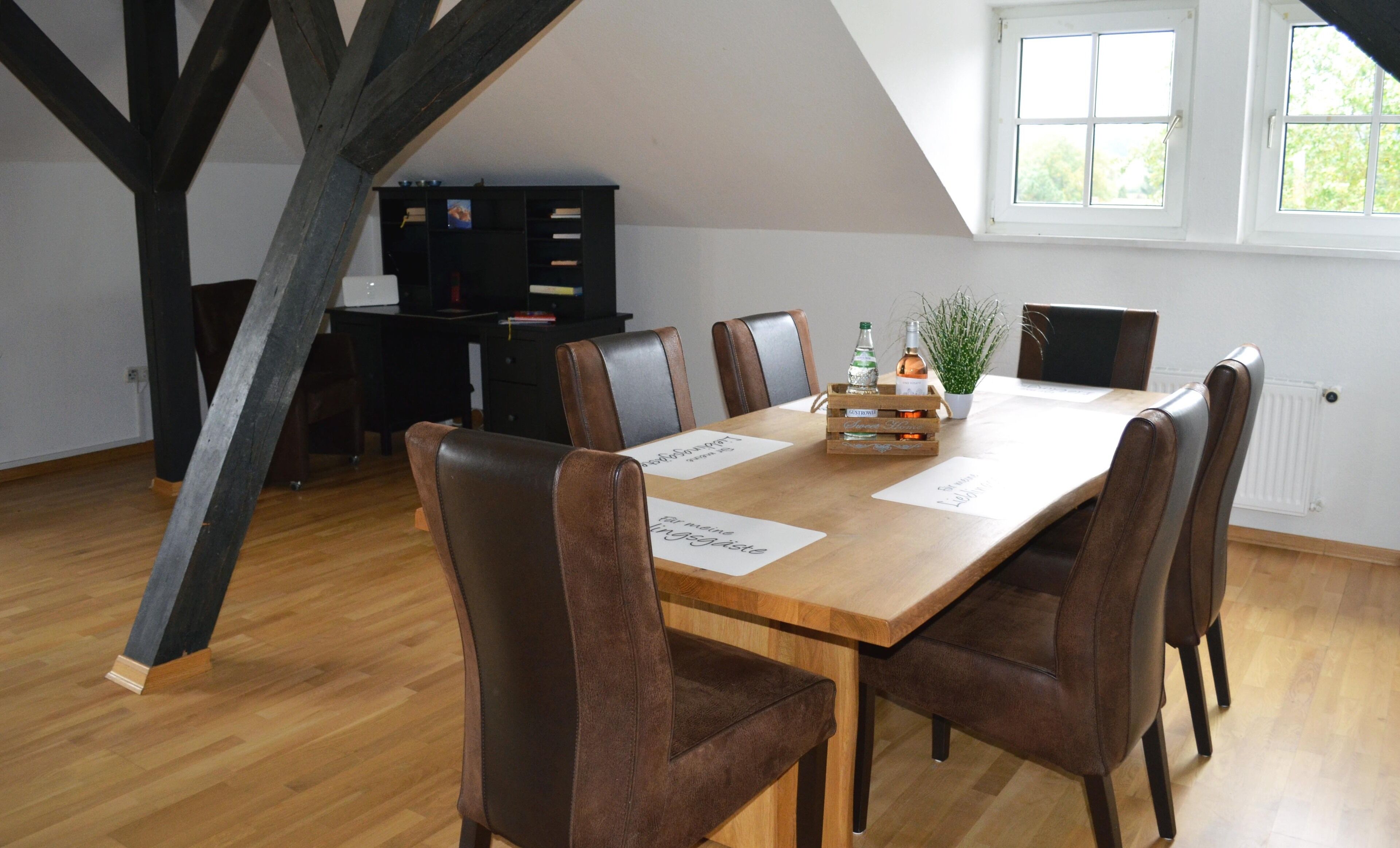 Un coin repas avec une table en bois, six chaises en cuir marron et un buffet noir en arrière-plan.