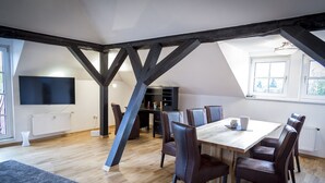 Un comedor con mesa de madera y sillas de cuero, una estantería negra y un televisor montado en la pared.