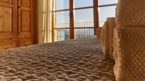 Un lit recouvert d’une couverture à motifs, des meubles en bois et une fenêtre donnant sur un balcon.