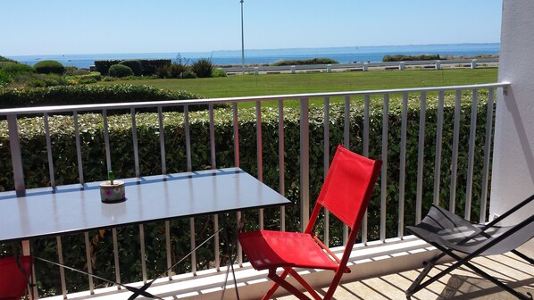 A balcony with a table and chairs, overlooking a grassy area and the sea. - New south-facing seafront apartment (classified 3*) in a secure residence (Quiberon)