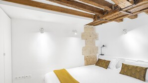 Ein Schlafzimmer mit einem großen Bett, weißen Wänden, freiliegenden Holzbalken und einer Steinwand.