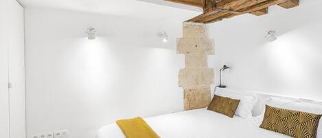 Ein Schlafzimmer mit einem großen Bett, weißen Wänden, freiliegenden Holzbalken und einer Steinwand.