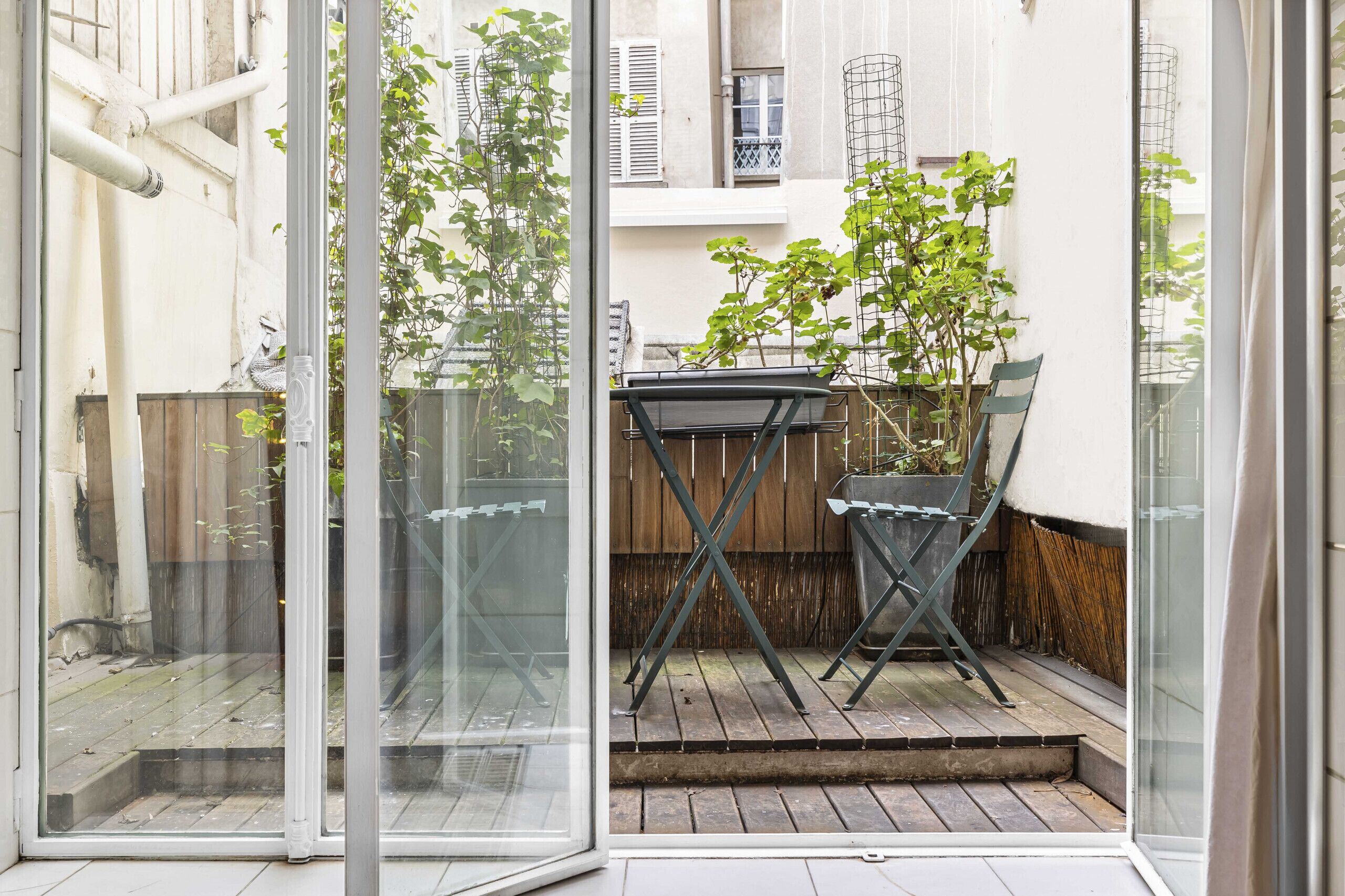 Une porte vitrée donnant sur un patio équipé d’une table et de chaises, ainsi qu’une clôture en bois et un pot de fleurs.
