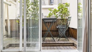 Eine Glastür führt zu einer Terrasse mit Tisch und Stühlen, einem Holzzaun und einem Blumentopf.